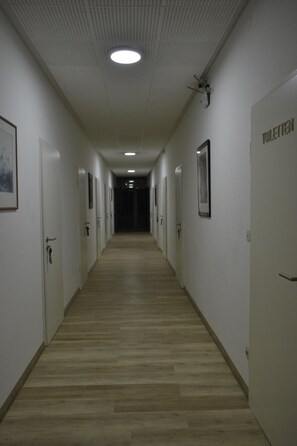 Un pasillo largo y estrecho con puertas a ambos lados, que conduce a una zona oscura al final.