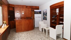 A reception area with a wooden reception desk, white chairs, a small table, and a wall with framed pictures. - Pension Highway 3 Sennestadt-Bielefeld (Bielefeld)