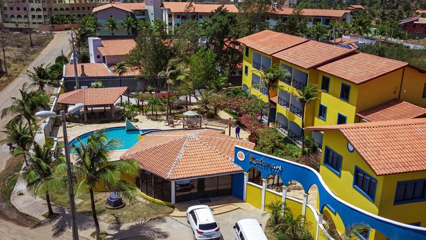 A multi-story hotel with a swimming pool, surrounded by palm trees and featuring a red-tiled roof.