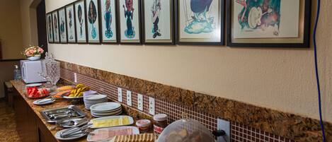 A long buffet table with various food items and a wall of framed caricature artwork.