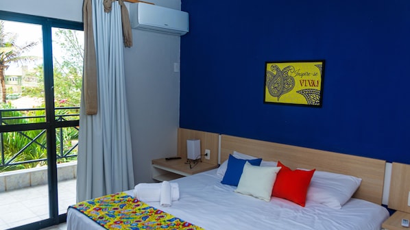 A hotel room with a bed, a bedside table, a wall-mounted air conditioner, a window with curtains, and a motivational poster on the wall. - Kalamari Beach Hotel (Aquiraz)