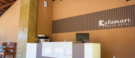 A reception desk at Kalamari Beach Hotel with a tiled wall and a wooden bench.