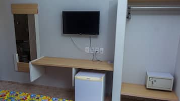 A room with a TV mounted on the wall, a small refrigerator, a cabinet, and a wooden shelf.