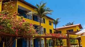 A yellow building with balconies, a palm tree, and flowering plants. - Kalamari Beach Hotel (Aquiraz)