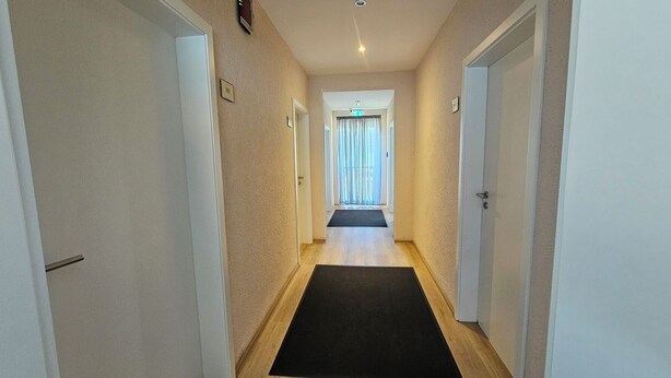 A hallway with a black mat, white doors, and a light-colored wall. - Pension Highway Bünde (Buende)