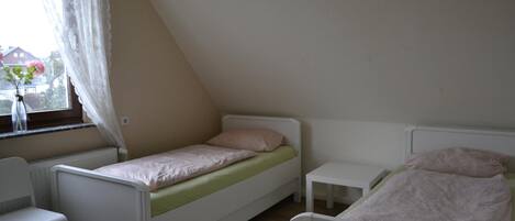 Una habitación pequeña con cama individual, techo inclinado, ventana con cortina y radiador.
