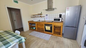 A compact kitchen with a microwave, oven, and refrigerator. There is a wooden countertop with shelves above and a sink. A table with a checkered tablecloth is visible. - Pension Highway Bünde (Buende)