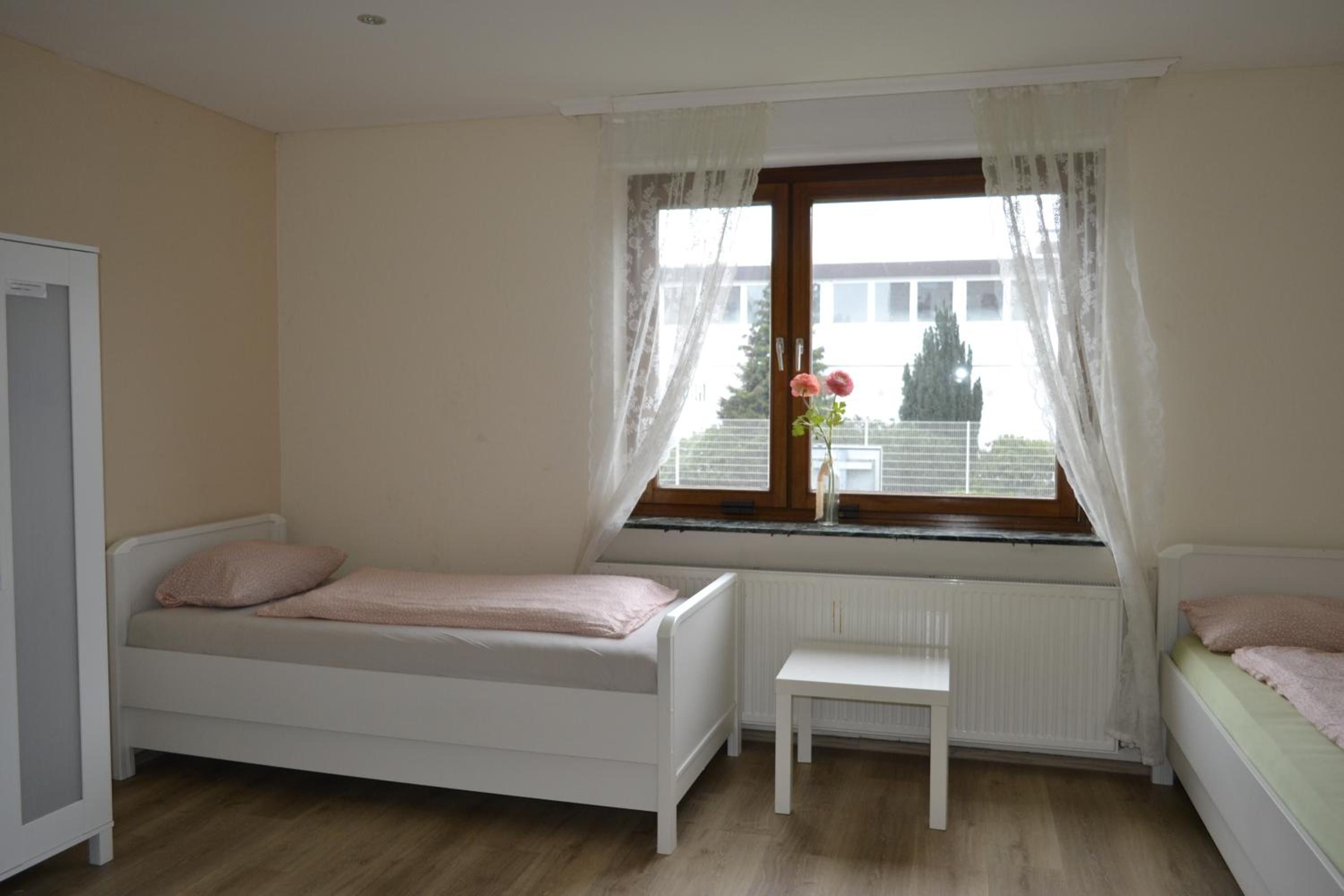 A small, single-bed room with a window, a radiator, and a white bench.