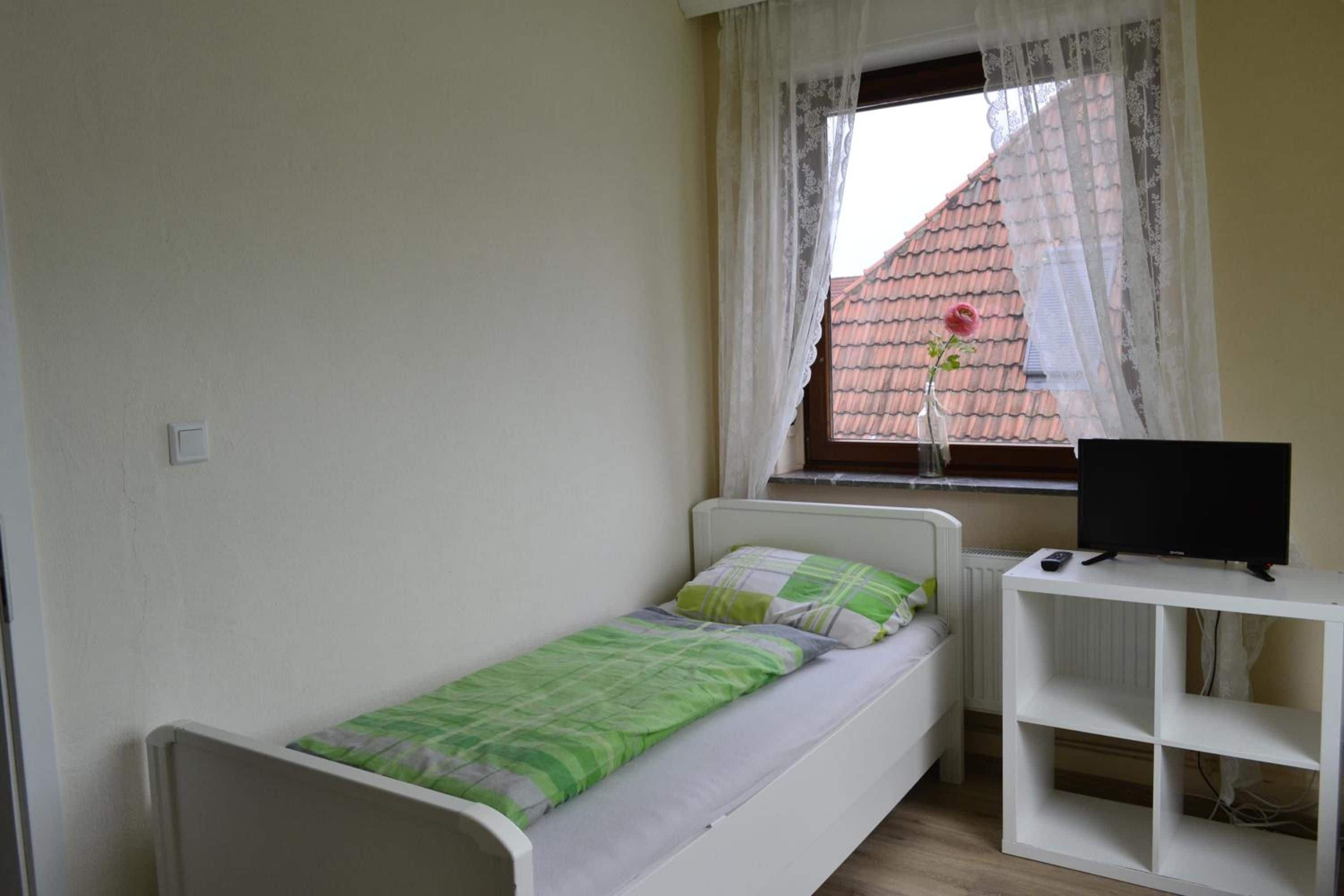 Une petite chambre avec un lit simple, une fenêtre, un bureau et un téléviseur.