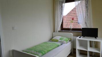 Une petite chambre avec un lit simple, une fenêtre, un bureau et un téléviseur.
