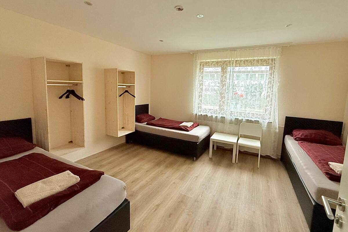 Ein Hotelzimmer mit zwei Betten, einem Kleiderschrank, einem Fenster mit Spitzenvorhängen und Holzdielen.