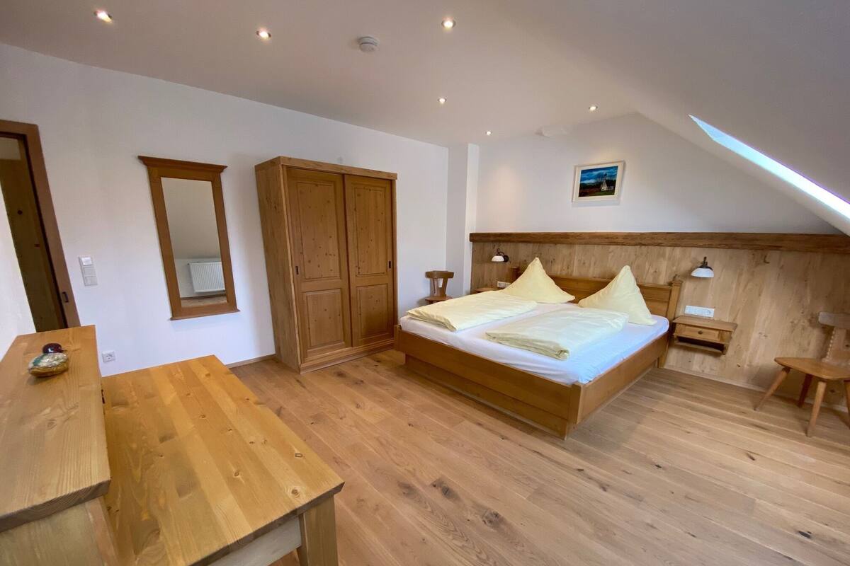 A bedroom with a wooden bed, a wardrobe, a desk, and a small table.
