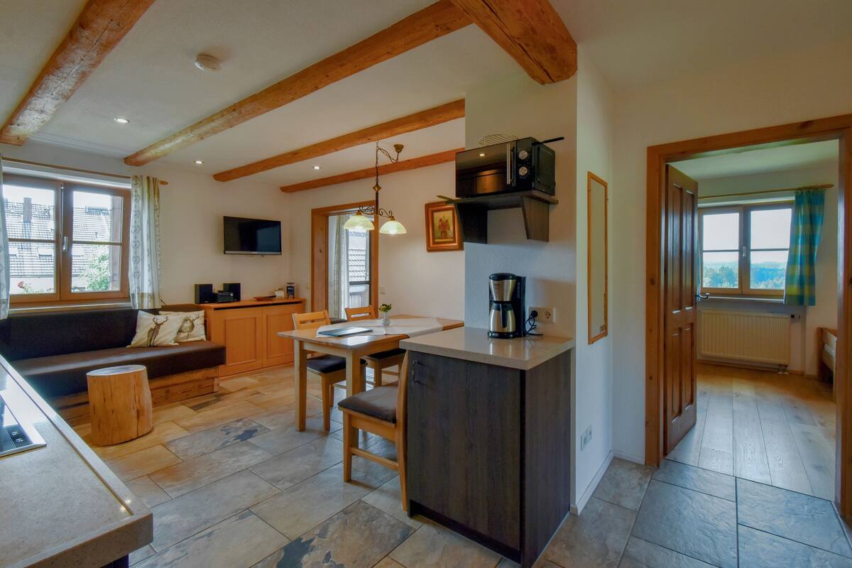 A cozy kitchen with wooden beams, a dining area, and a view through a window.
