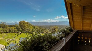 A wooden balcony with a view of a green landscape and mountains in the distance. - Biohof-Rechenmacher (Uffing am Steffelsee)