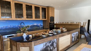 A modern kitchen with wooden cabinets, a large island with a black countertop, and a scenic mountain view on the wall. - Biohof-Rechenmacher (Uffing am Steffelsee)
