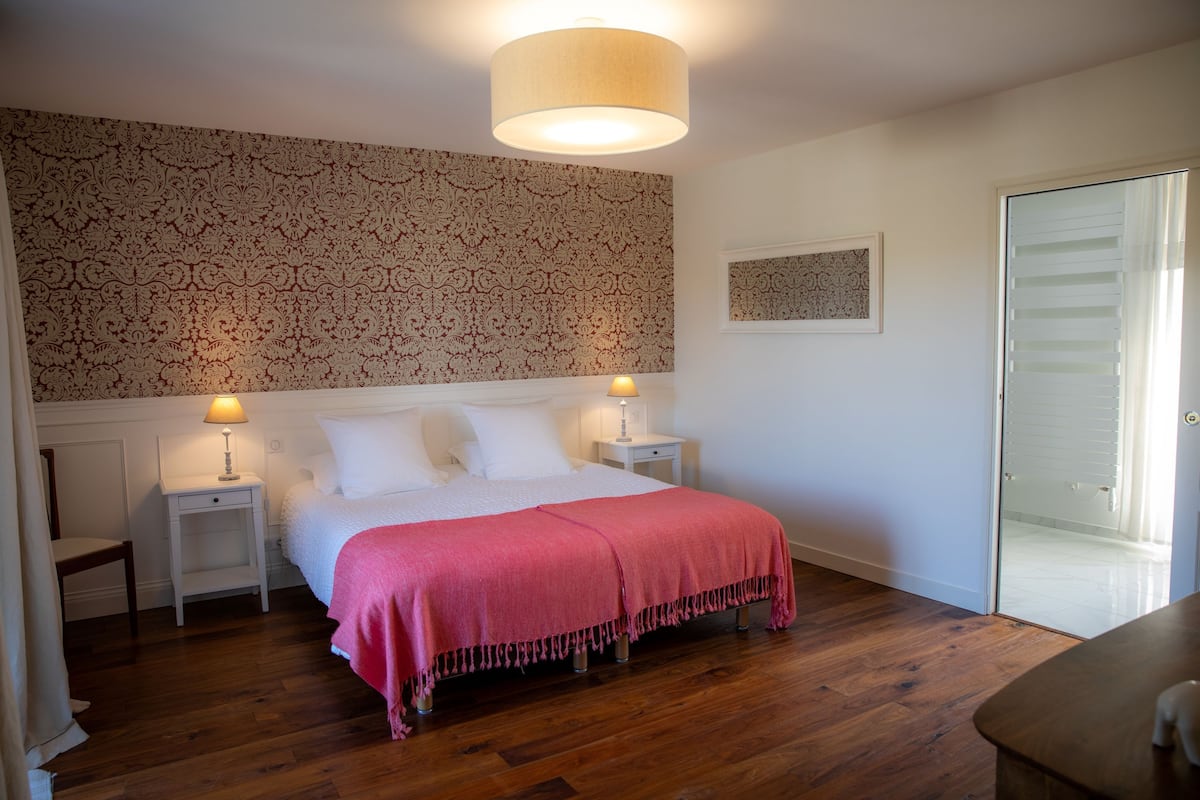 A bedroom with a bed, two bedside tables, a nightstand, a door, and a patterned wallpaper.