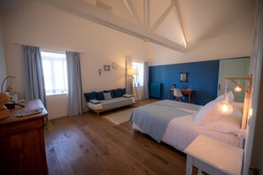 Un dormitorio con una cama grande, un aparador de madera, un escritorio con una silla, una pared de acento azul y una ventana con cortinas.