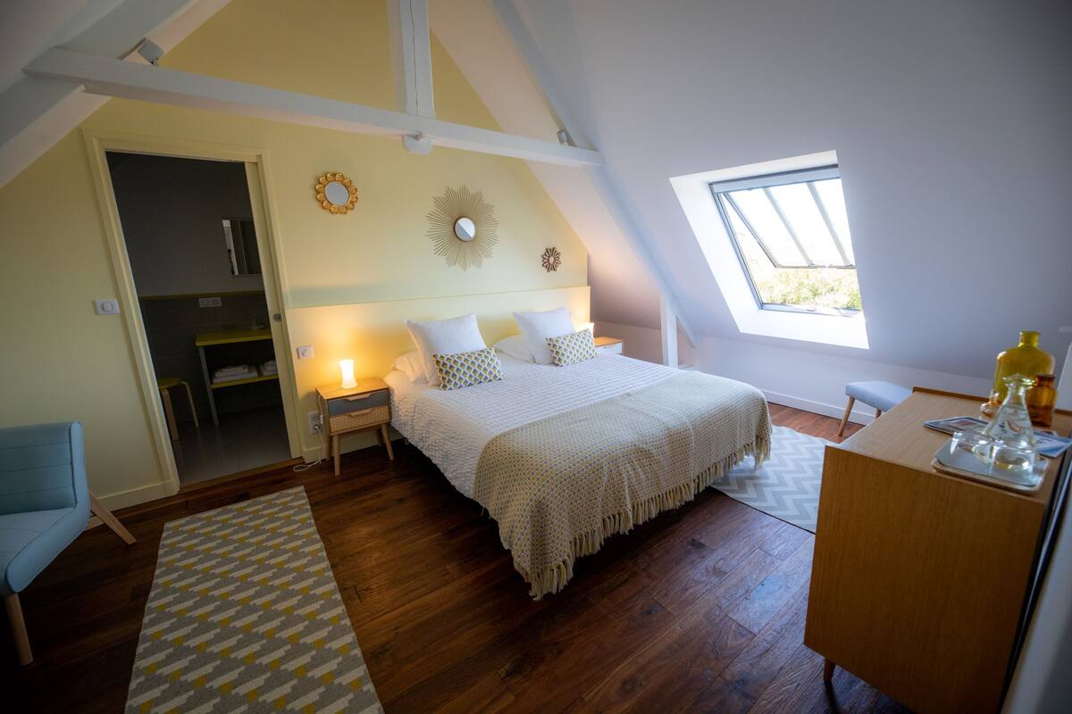 A bedroom with a bed, bedside tables, a desk, a chair, a window, and a skylight.