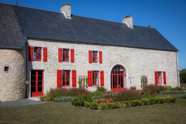Un edificio de piedra con contraventanas rojas y tejado negro.