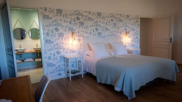 A bedroom with a bed, bedside tables, a nightstand, a mirror, a bathroom with a sink, and a door.