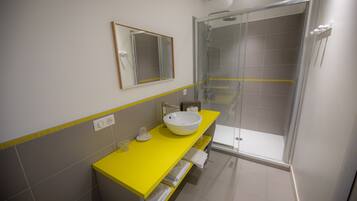 Een moderne badkamer met een geel aanrecht, een witte wastafel en een douche met glazen wanden.