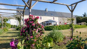 Un edificio de piedra con un porche cubierto y un jardín con rosas rosadas.