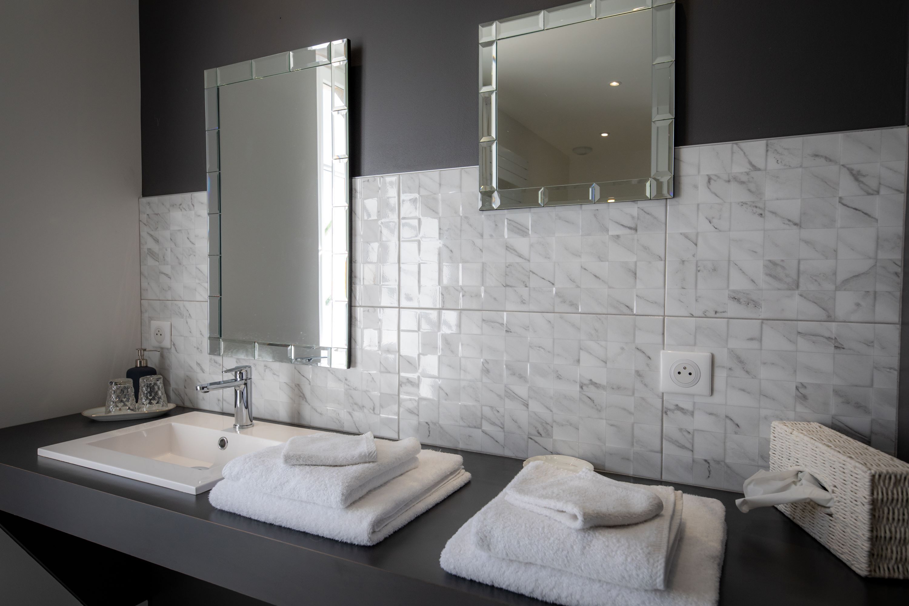 A modern bathroom with a white marble sink, two mirrors, and neatly folded towels.
