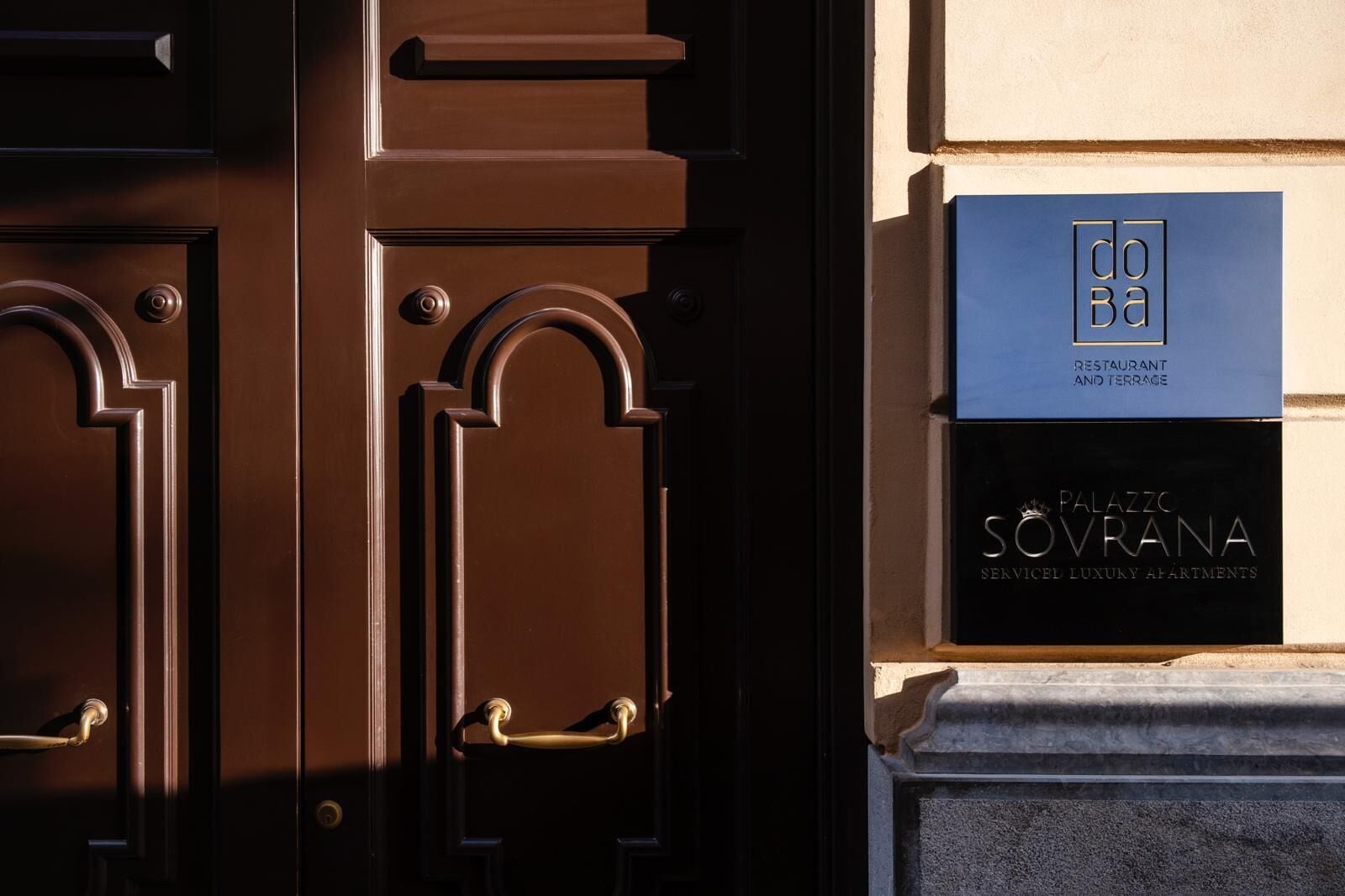 A brown door with two handles and a blue and black sign with 'DOBA RESTAURANT AND TERRACE' and 'PALAZZO SVRANA SENICEL LUXURY APARTMENTS'.