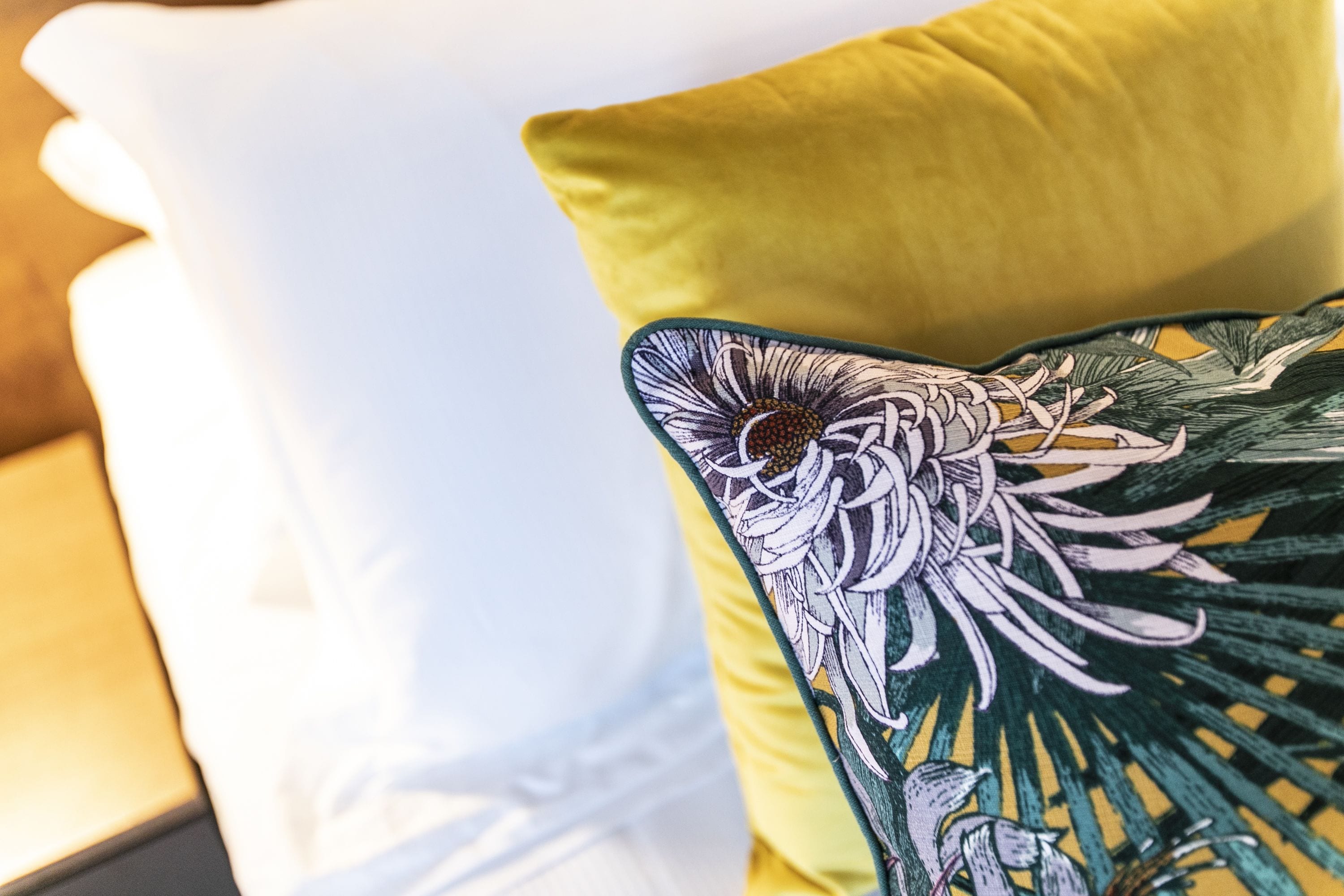 A close-up of a bed with a white pillow and a yellow pillow with a floral design.