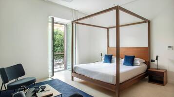 A modern bedroom with a four-poster bed, a desk with a chair, and a view of the outdoors through a sliding glass door.