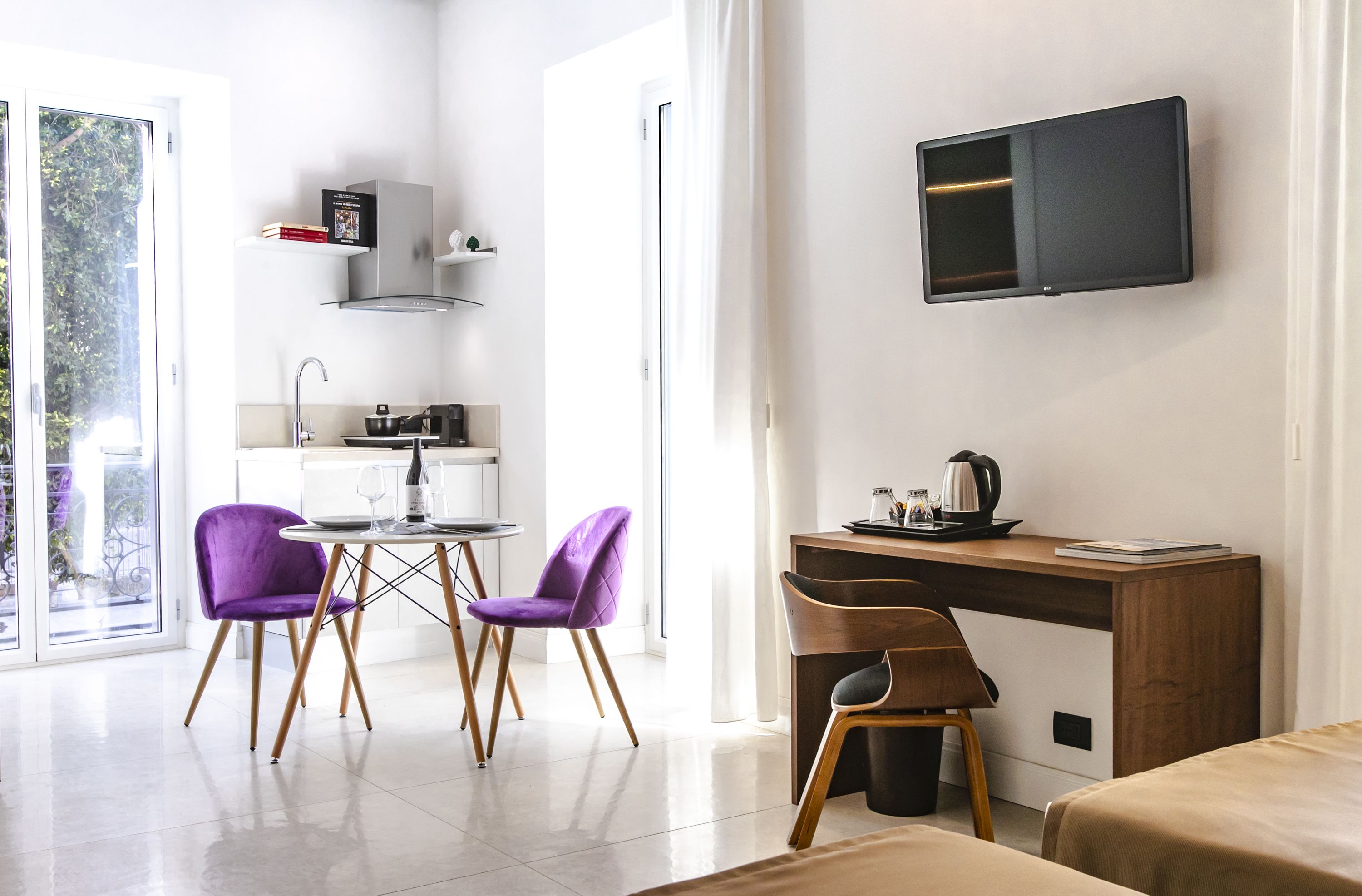 Ein modernes Hotelzimmer mit Essbereich, Küchenzeile und einem an der Wand montierten Fernseher.