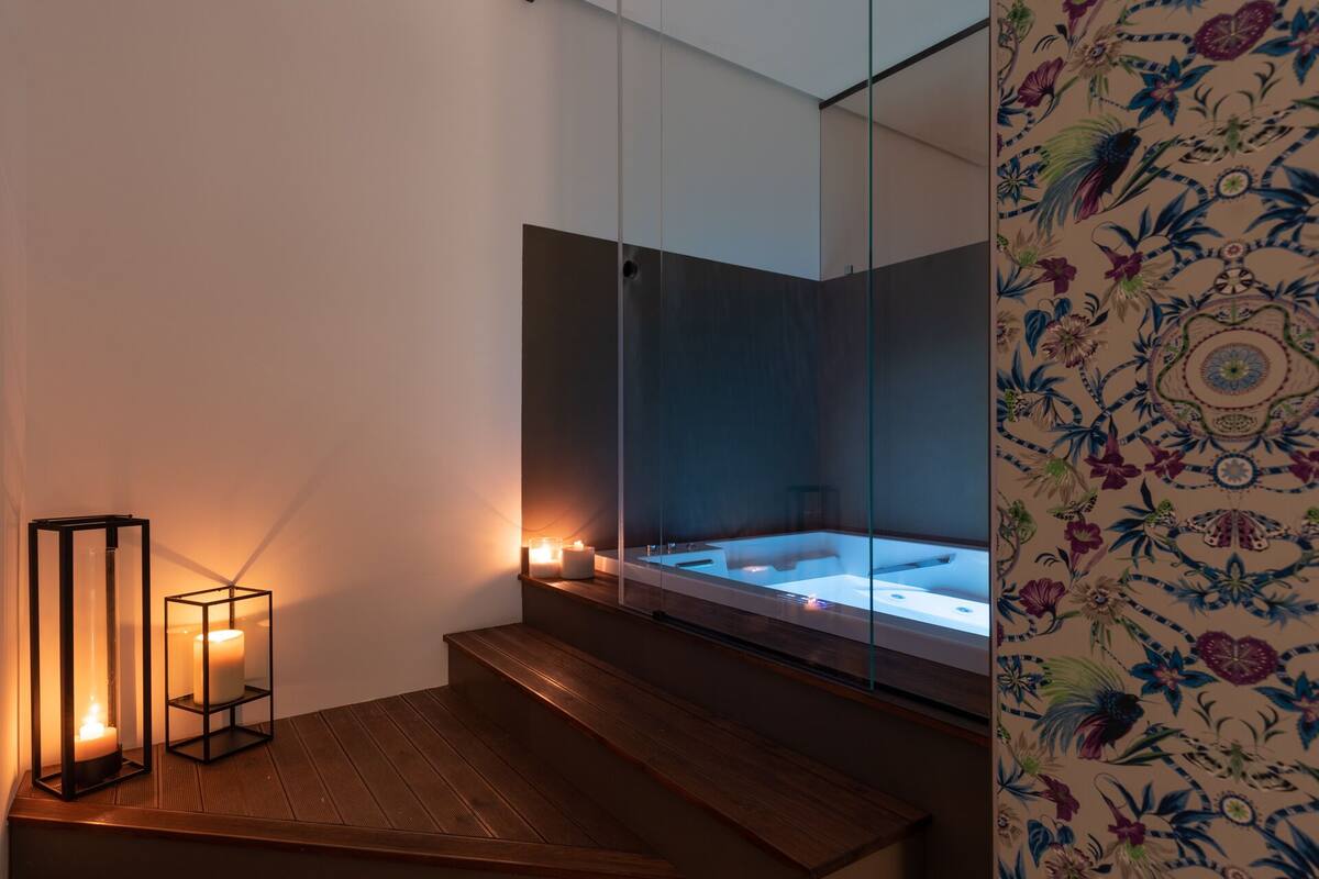 A modern bathroom with a glass-enclosed bathtub, wooden steps, and candles.