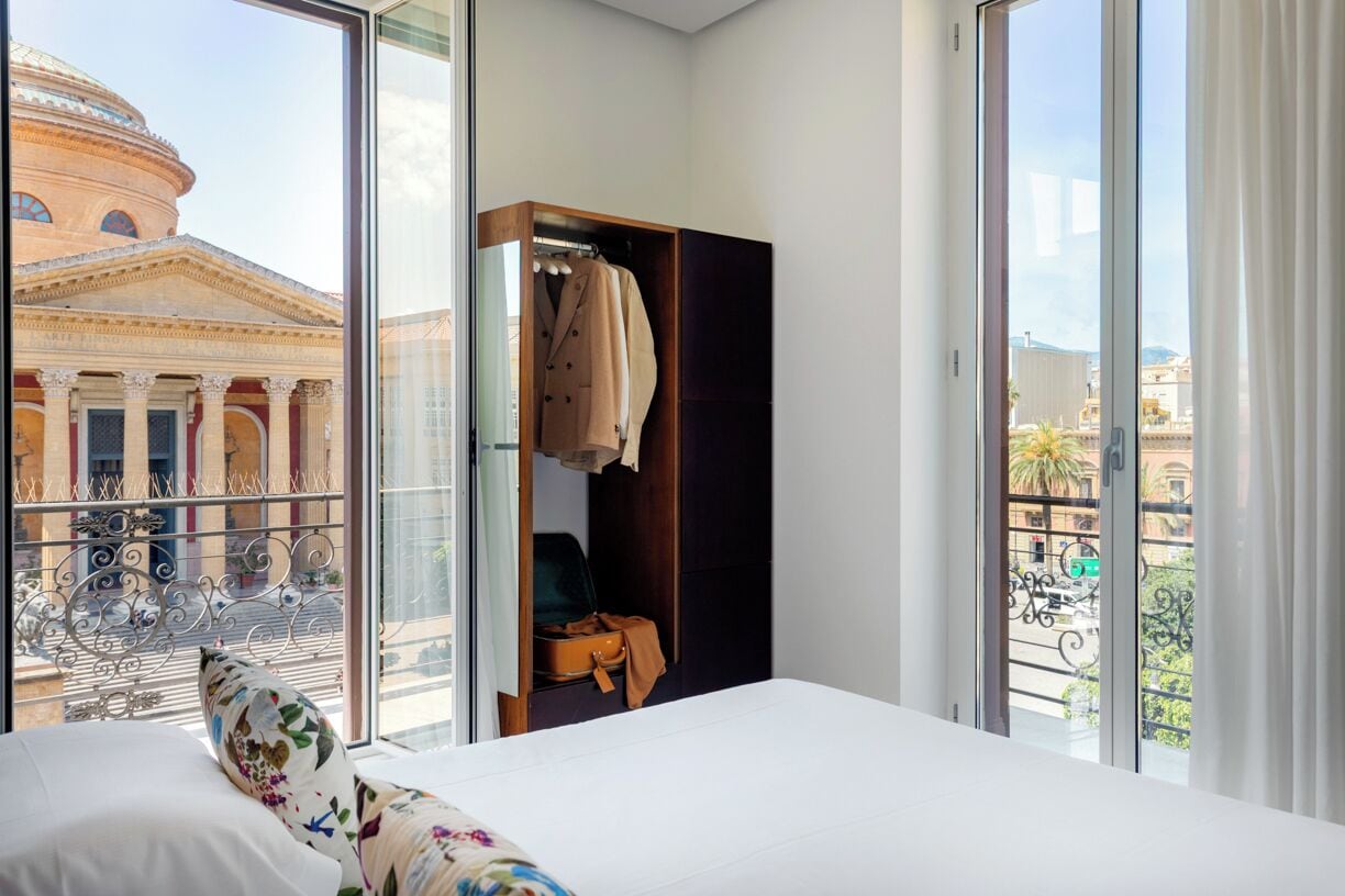 Habitación de hotel con un ventanal grande, cama, armario y vistas a un edificio con columnas.