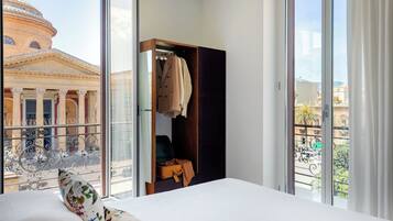 Habitación de hotel con un ventanal grande, cama, armario y vistas a un edificio con columnas.