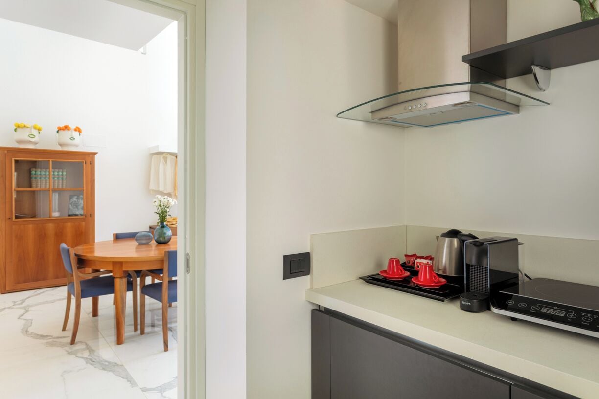 A compact kitchen with a modern stove, a glass shelf, and a dining area with a wooden table and chairs.