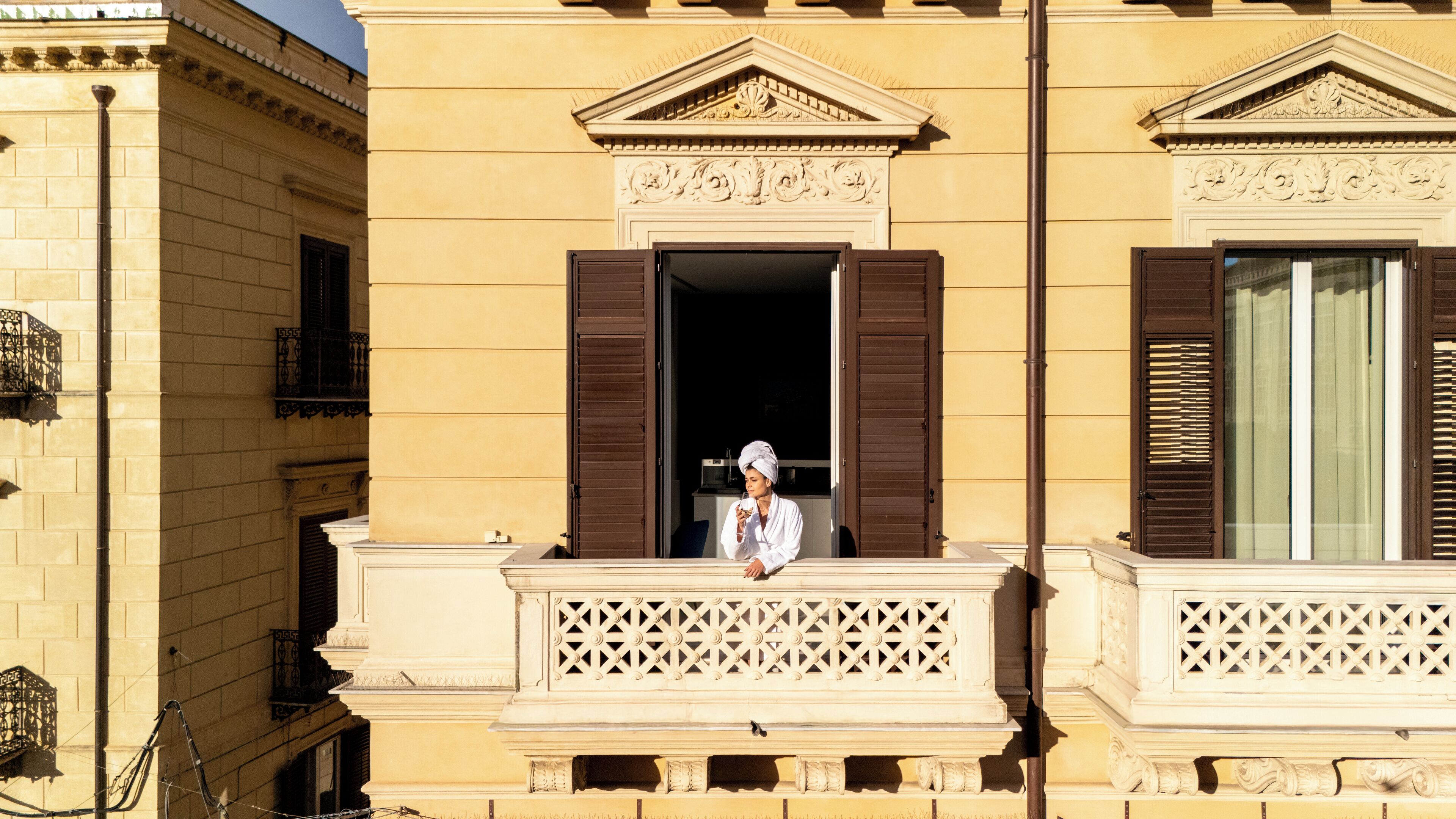 Un edificio con balcón, una ventana con persianas marrones y una barandilla decorativa.
