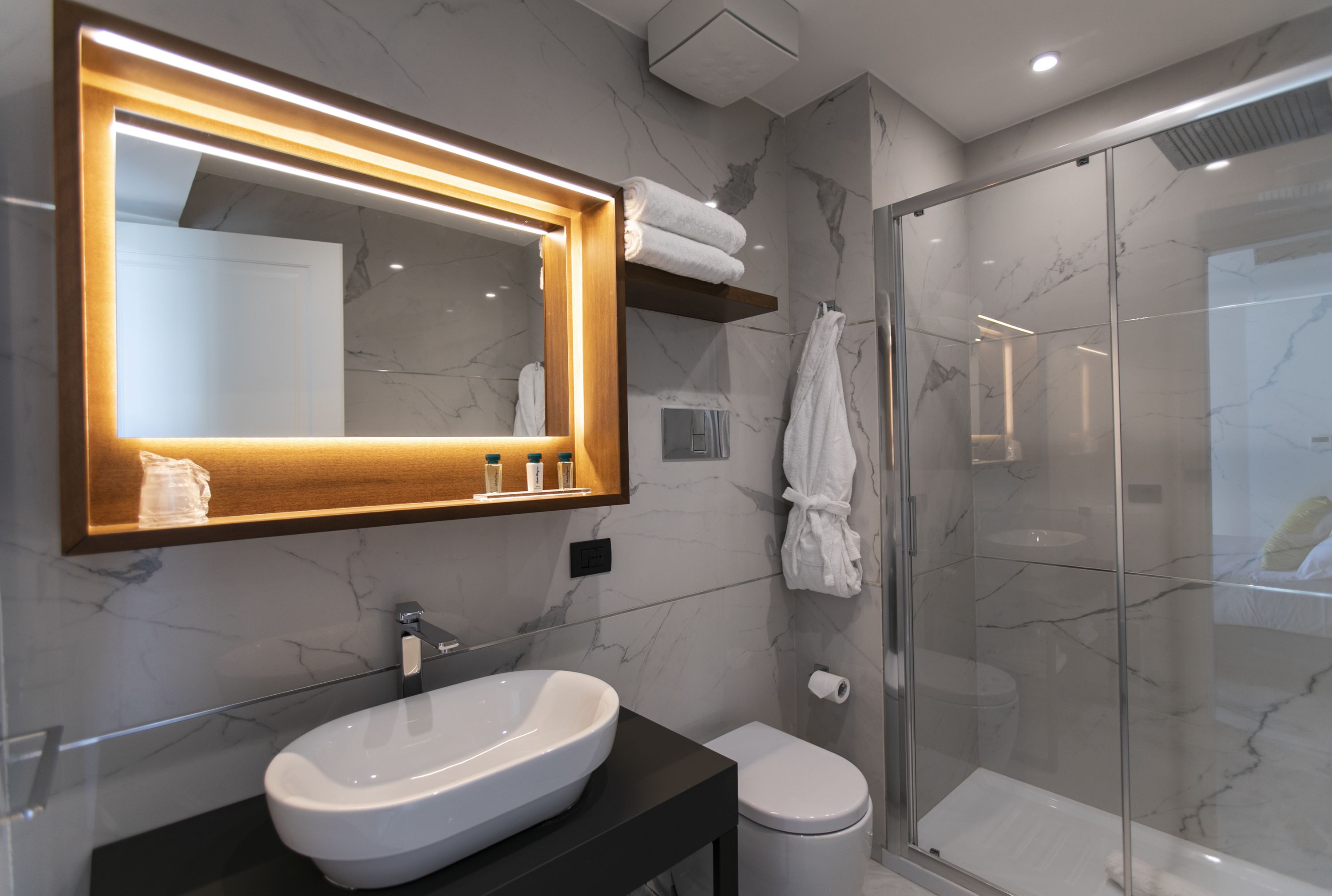 A modern bathroom with a large mirror, a vessel sink, a toilet, and a glass-enclosed shower.