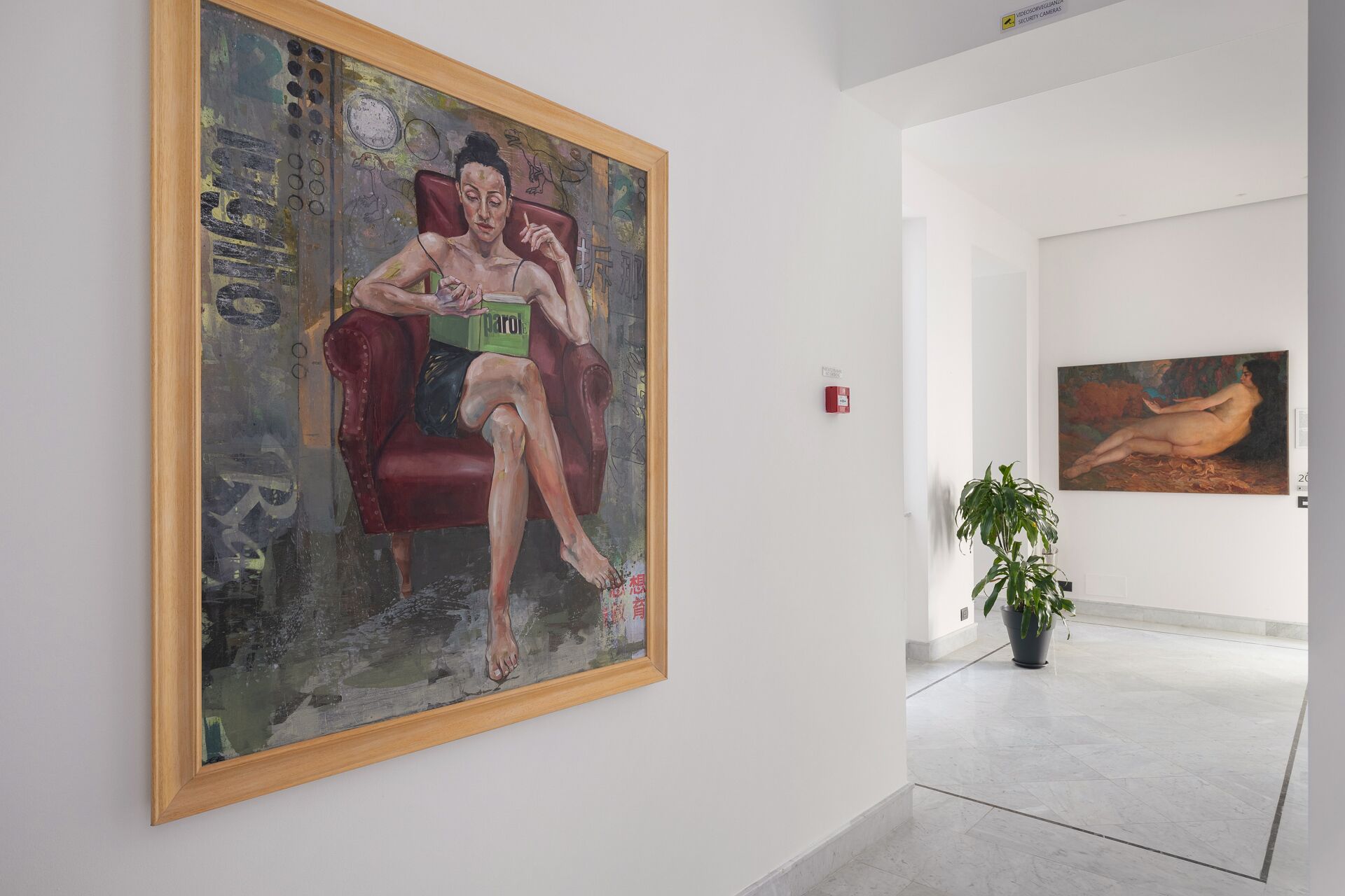 An art gallery with a large painting of a woman on a red chair, a smaller painting on the wall, and a potted plant in the foreground.