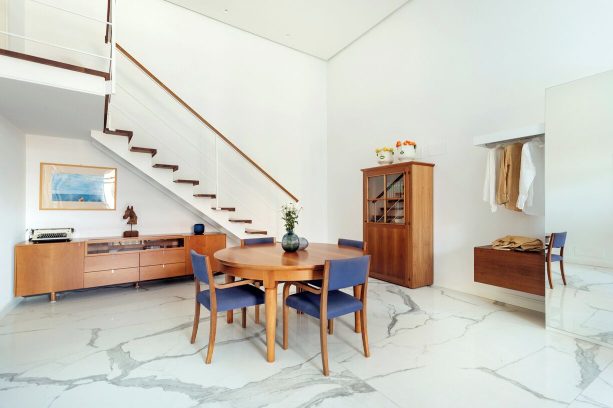 A modern interior with a dining area, a staircase, and a wooden cabinet.
