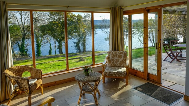 Una habitación con ventanas amplias, mobiliario de mimbre y vistas a un lago.
