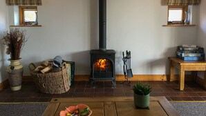 Una sala de estar acogedora con una estufa de leña, una chimenea, una mesita con libros y un jarrón con flores secas.