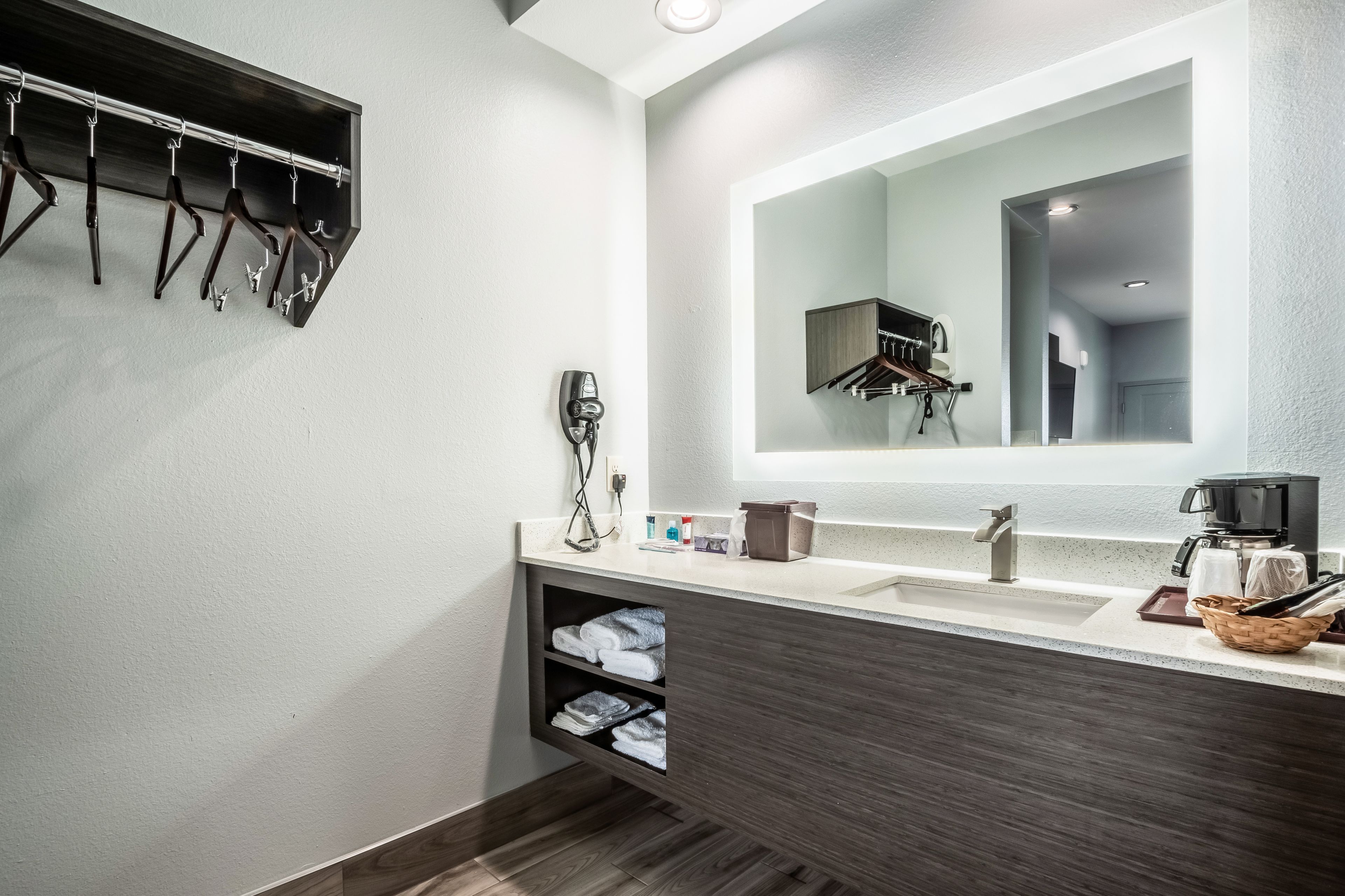 A modern bathroom with a large mirror, a towel rack, a coffee machine, and a sink.