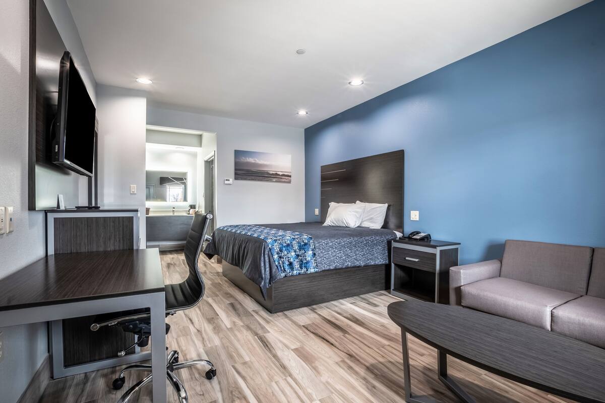 A modern hotel room with a large bed, a desk, a chair, a sofa, and a TV.
