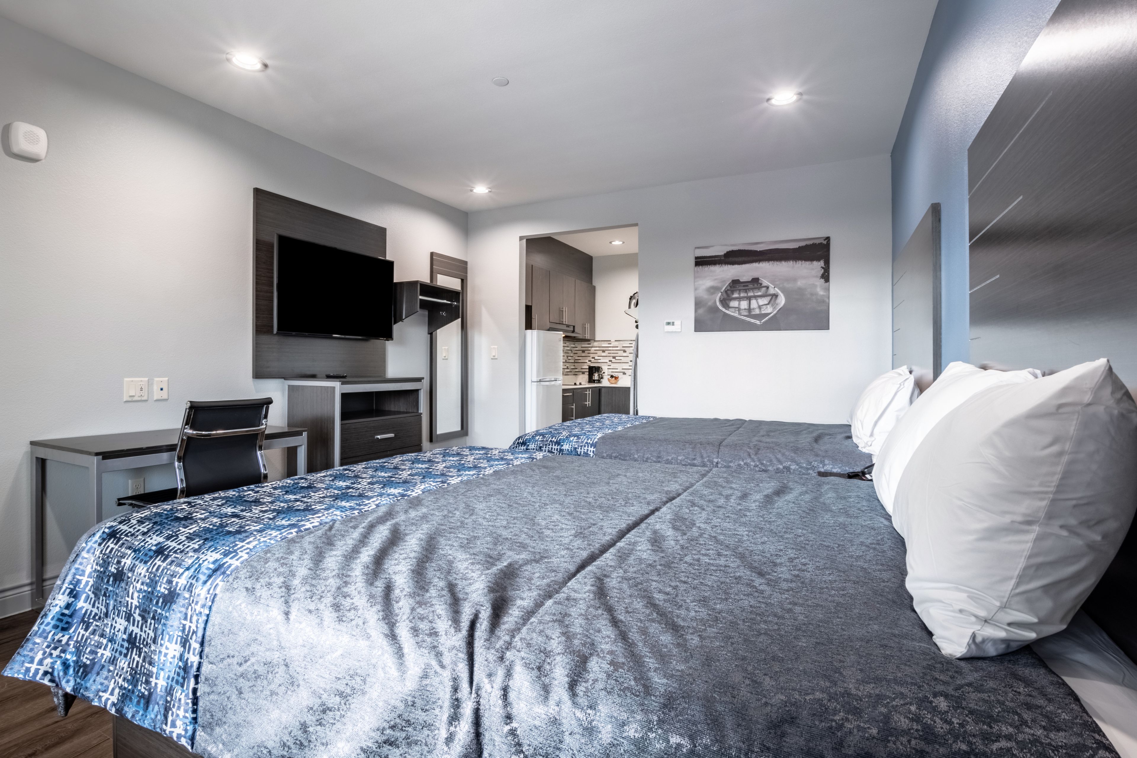 A modern hotel room with a large bed, a desk, a flat-screen TV, and a kitchenette.