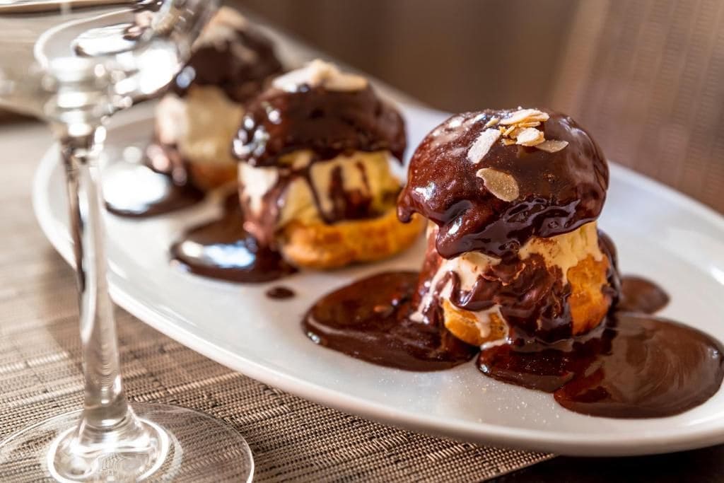 Een nagerechtenbord met chocolade-bedekte ijs en amandelen, vergezeld van een glas wijn.