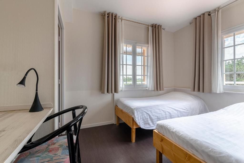 A bedroom with two single beds, a desk with a chair, and a window with curtains.