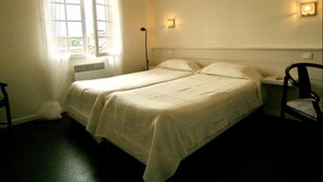 Un lit simple avec une couvre-lit blanche, une table de chevet avec une lampe et une chaise.