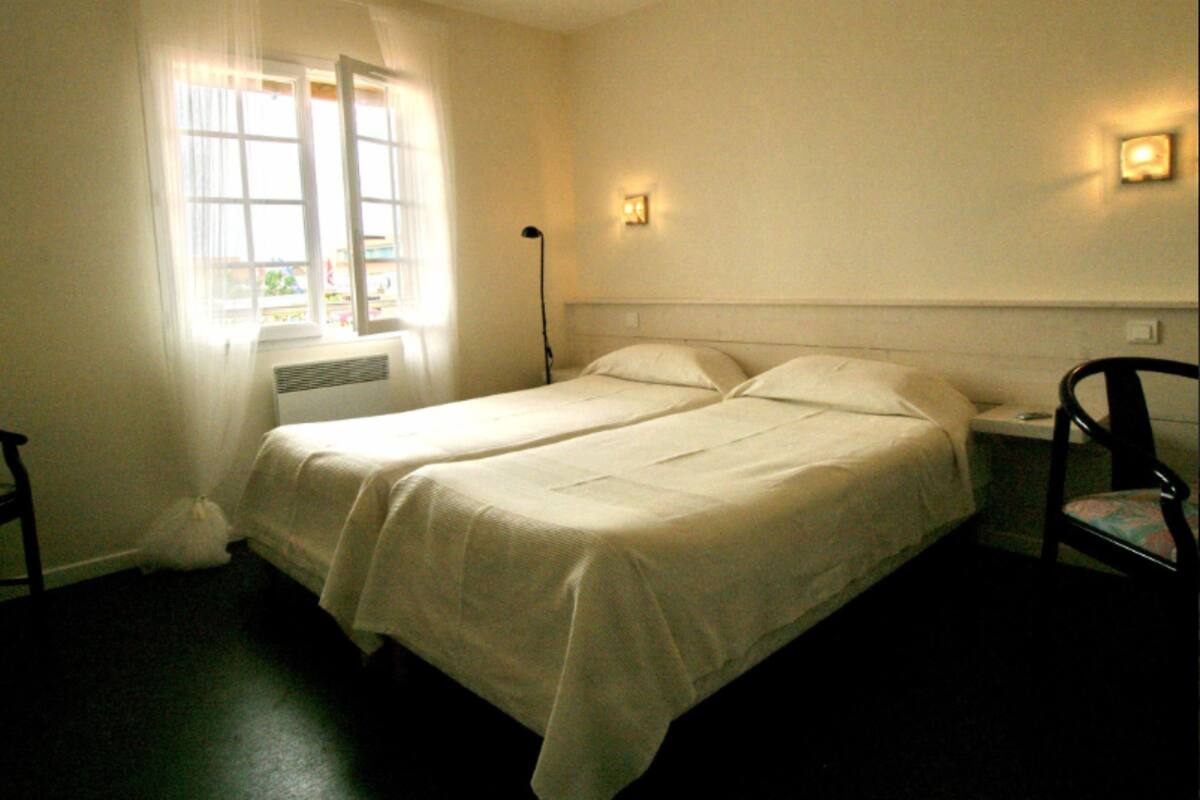 A twin bed with a white bedspread, a nightstand with a lamp, and a chair.