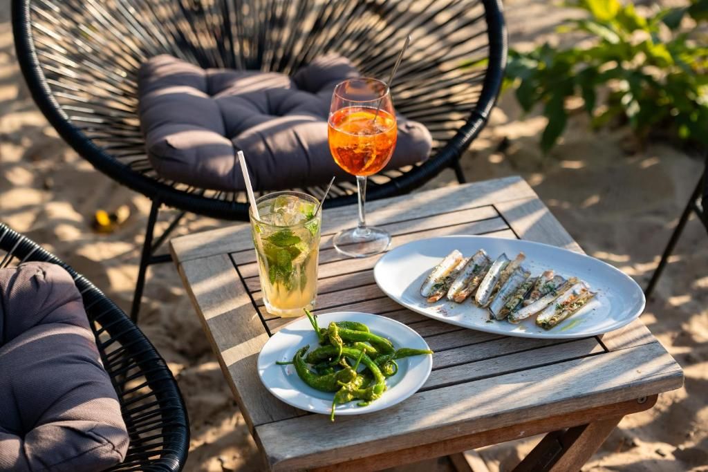 Een houten tafel met een bord gegrilde vis, een glas sinaasappeldrank en een bord groene paprika's.