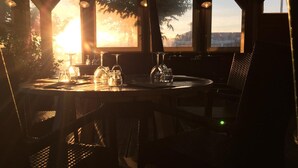 Une table dressée pour deux personnes, avec vue sur le coucher de soleil à travers de grandes fenêtres.